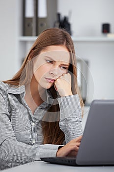 Bored young business woman working with laptop.