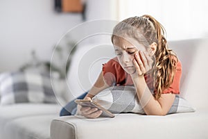 Bored young girl finds no more joy in scrolling on her phone as she sits at home on a couch