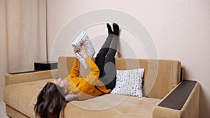 Bored young woman in sweater lies on sofa throwing pillows