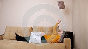 Bored young woman in sweater lies on sofa throwing pillows