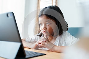 Boring asian girl is studying online via the internet on tablet while in the living room at home morning, Asian elementary school