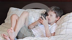 Boring boy laying on bed and playing on mobile phone