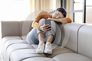 Boring Content. Bored indian woman with smartphone sitting on couch at home