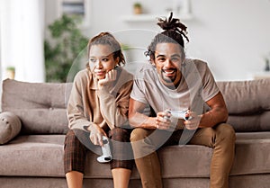 Boring date. Excited african american man playing video game and ignoring bored woman sitting beside photo