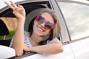 Boring days behind me, brighter days ahead. a young woman wearing showing a peace sign out of a car window on a road