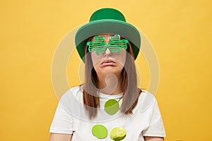 Boring leprechaun-themed holiday party. Crying unhappy woman wearing green leprechaun hat and shamrock glasses posing isolated on