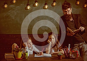 Boring lesson concept. Teacher and girls pupils in classroom, chalkboard on background. Man with beard teaches