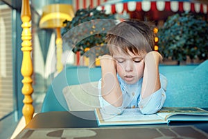 Boring and tired little boy reading book