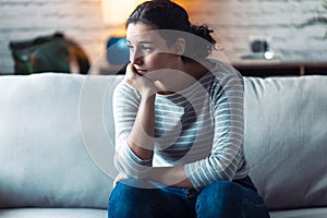 Boring young woman looking to side and thinking while sitting on the sofa at home