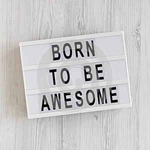 `Born to be awesome` words on a lightbox on a white wooden background, top view. Overhead, from above, flat lay