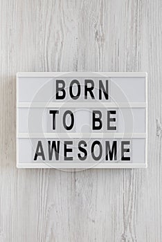 `Born to be awesome` words on a modern board on a white wooden background, top view. Overhead, from above, flat lay. Close-up