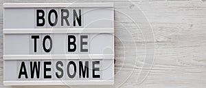 `Born to be awesome` words on a modern board on a white wooden surface, top view. Overhead, from above, flat lay. Space for text