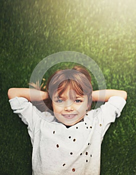 Born to be happy. a cute little girl smiling while lying down on grass.