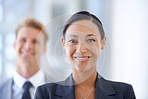 Born to be a leader. A businesswoman smiling at the camera with her male colleague in the background.