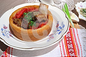 Borsch soup with meat in bread loaf on plate in photo