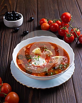 Borscht with lemon and olives in a white plate on a wooden table.