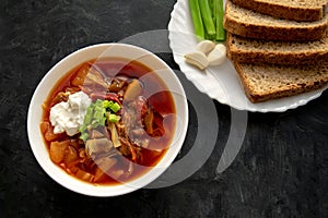 Borscht soup in a white bowl with black bread, green onion and garlic on dark gray background. Famous traditional Ukrainian and Ru