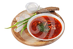 Borscht with sour cream, green onions, bacon and rye bread on a round wooden Board on white background