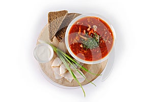 Borscht with sour cream, green onions, bacon and rye bread on a round wooden Board on white background, top view