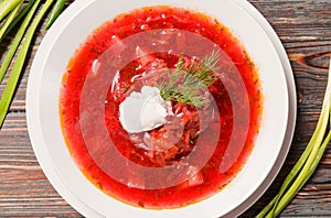 Borscht with sour cream and herbs on a wooden background, top view