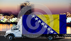 Bosnia and herzegovina flag on the side of a white van against the backdrop of a blurred city and river. Logistics concept