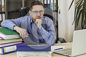 Boss businessman at his desk in the office with a bunch of folders with papers. Strenuous office work. Preparing of report