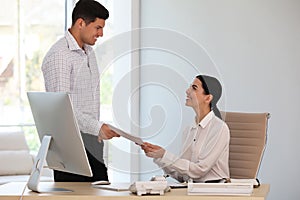 Boss giving papers to secretary in office