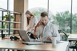 Boss is having conversation by the phone. Man and woman are working in the modern office together