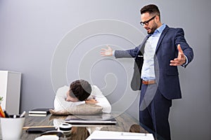 Boss Looking At Tired Employee Sleeping At Office