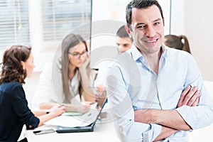 Boss in the office, his team having meeting in background