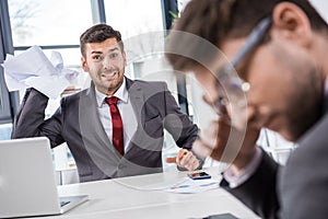 Boss throwing papers at upset colleague at business meeting