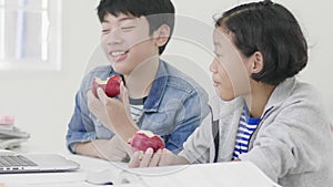 Both children  are eating apples. And also do homework