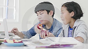 Both children  are eating apples. And also do homework