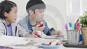 Both children  are eating apples. And also do homework