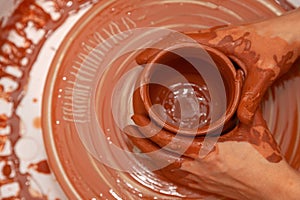 With both hands, a master potter shapes an earthen vessel rotating on a potter`s wheel Top view