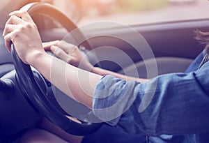 Both hands of woman wearing a blue jean shirt gripping wheel driving right hand drive car