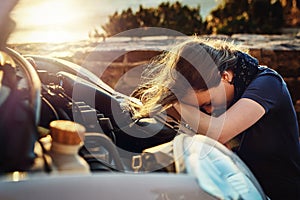 Both her and her car are going through a breakdown. a young woman looking upset after breaking down on the roadside.