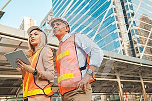 Both male and female engineers wear helmets. Standing in the construction zone while the female engineer was holding the tablet