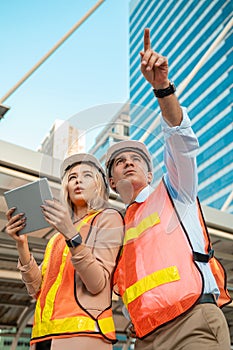 Both male and female engineers wear helmets. Standing in the construction zone while the female engineer was holding the tablet