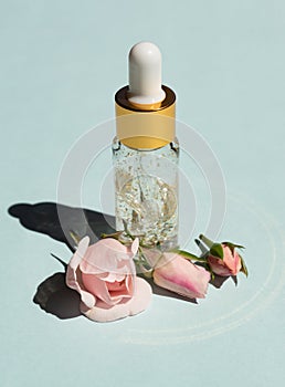 Bottle of 24k gold serum on a blue background with rose flowers. The concept of skin care at home