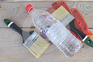 A bottle of acetone - two paintbrushes and gloves in the background - wooden background - Construction concept