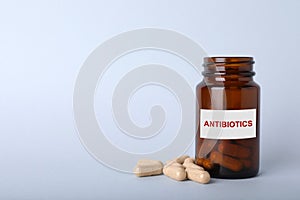 Bottle with antibiotic pills on light grey background, space for text