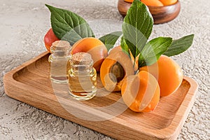 bottle of apricot kernel oil on a wooden tray with ripe fruit and a gray cement background. organic skin care.