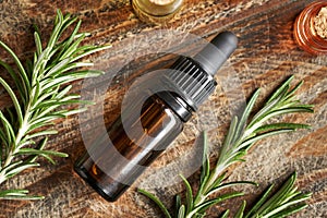A bottle of aromatherapy essential oil with with a black cap with fresh rosemary twigs on a table
