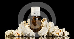 Bottle of aromatic liquid for electronic cigarettes, handful of popcorn nearby, isolated on black