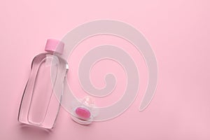 Bottle of baby oil and pacifier on pink background, flat lay. Space for text