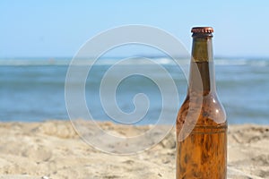 Bottle of beer on beach near sea, closeup. Space for text