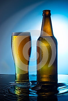 bottle of beer with a glass of foamy beer on a blue background, on the water