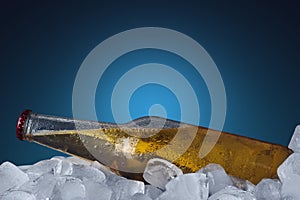 Bottle of beer in ice cubes at the blue background