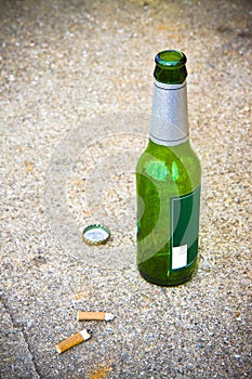 Bottle of beer resting on the ground with three cigarette's